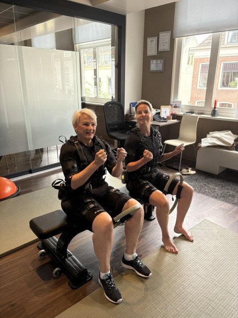 Twee deelnemers zitten naast elkaar op een trainingsbank met hun EMS-pakken aan