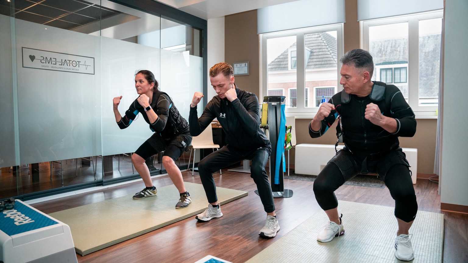 Twee deelnemers doen onder begeleiding van hun EMS coach EMS-oefeningen in de Total EMS-studio